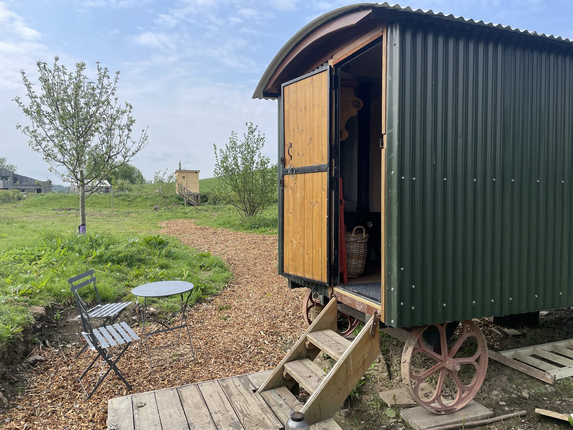 Dark green shepherd's hut exterior with open door, wooden steps and iron wheels